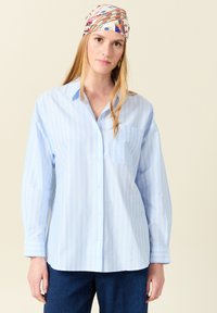 Camicia button-up azzurro chiaro con sottili righe bianche, una tasca sul petto e maniche lunghe; realizzata in morbido cotone.