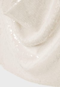Tissu doux beige clair avec une texture tricotée fine et de petits sequins blancs dispersés créant un effet subtil de scintillement.
