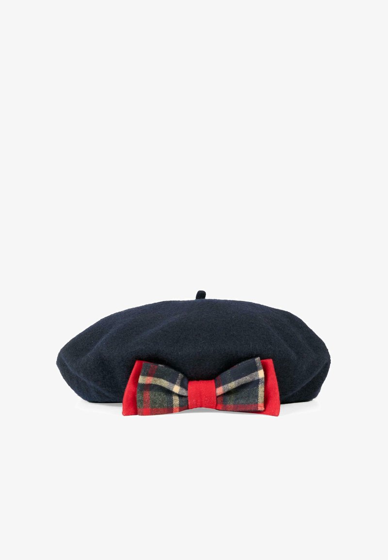 Beret en laine bleu marine avec un nœud rouge à carreaux. Caractérisé par une forme ronde et un bouton sur le dessus pour un maintien sécurisé.