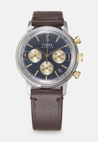 Montre Timex Marlin avec un cadran bleu marine, des accents dorés, trois sous-cadrans et un bracelet en cuir marron. Boîtier en acier avec des marquages de tachymètre.