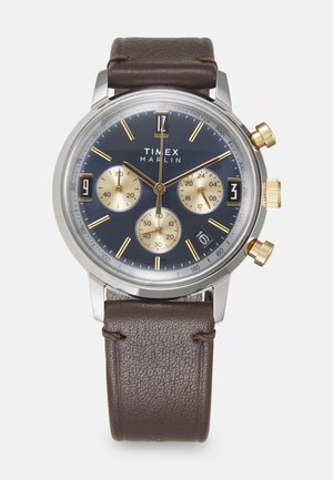 Zegarek Timex Marlin z granatową tarczą, złotymi akcentami, trzema subtarczami oraz brązowym skórzanym paskiem. Stalowa koperta z oznaczeniami tachymetru.