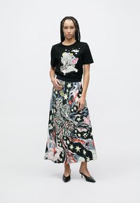 Camiseta negra con motivos coloridos de animales y estrellas, combinada con una falda larga hasta el suelo que presenta patrones abstractos vibrantes y detalles.