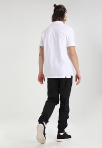 Bílá polo košile s krátkými rukávy, v kombinaci s černými joggingovými kalhotami a černými teniskami. Hladká tkanina s volným střihem.