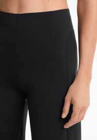 Fekete, magas derekú leggings, sima anyagból készült, oldalsó zsebekkel és testhezálló fazonnal, lapos derékkal és láthatatlan varrásokkal.