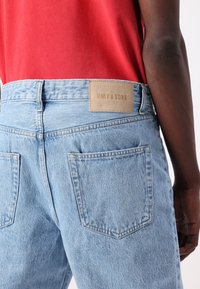Jean en denim bleu clair avec une coupe droite, doté d'une étiquette en cuir marron portant la mention "ONLY & SONS" et de poches arrière classiques.