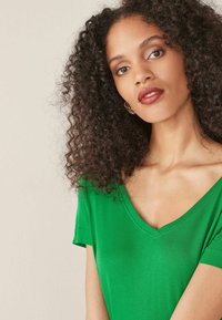 Zielona koszulka typu V-neck wykonana z miękkiego materiału, z krótkimi rękawami i luźnym fasonem. Gładka tekstura z minimalnymi detalami.