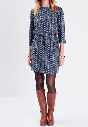 Korte mouw jurk in donkere stof met kleurrijk bloemenpatroon, taille ingesnoerd. Een paar bruine kniehoge laarzen maakt de look compleet.