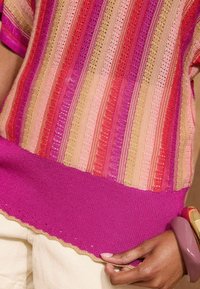 Sweter z pionowymi paskami w różowym, czerwonym i złotym kolorze, z falbaniastym dołem i jednolitym różowym wykończeniem na dole. Teksturowana tkanina.