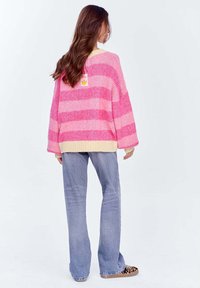 Różowy i jasnoróżowy w paski, duży sweter dzianinowy z kremowym wykończeniem, połączony z jasnoniebieskimi spodniami dzwonami i butami w panterkę.