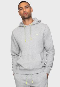 Grijze hoodie van zachte stof met een kangoeroezak, trekkoorden met gele accenten en een klein logo op de borst.