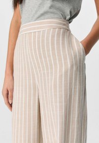 Lichtbeige wijde pijpen broek met witte verticale strepen, met een platte tailleband en zijzakken, gemaakt van een textuurstof.
