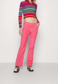 Pull court rayé rouge et vert à manches longues et col, associé à un jean flare en velours côtelé rose et des chaussures multicolores.