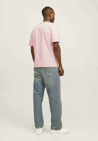 Pink cotton t-shirt with short sleeves, paired with loose-fitting light blue denim jeans. Model is facing away from the camera.