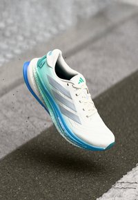 Baskets de course blanches avec des accents turquoise, trois rayures argentées, tige en maille texturée et semelle intermédiaire bleue. Design léger pour la performance.