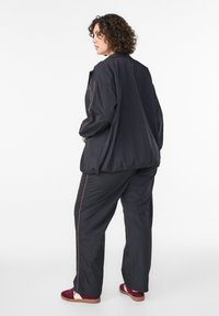 Schwarzes Set aus leichter Jacke und Hose mit elastischen Bündchen und lockerem Schnitt. Pinkfarbene Akzentnähte entlang der Kanten und Seitennähte.