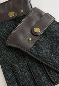 Hallid villa- ja nahkkindad tumedate pruuni nahkdetailidega, millel on messingist trukid ja tekstuuriga viimistlus.