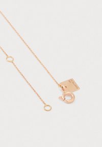 Sart rose gold kæderekæde med fjederlås og rektangulær plade gravet med "18K GINETTEN" på en ensfarvet hvid baggrund.
