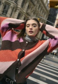 Multicolored knitted cardigan featuring bold stripes in orange, pink, purple, and brown, with round buttons and a soft texture.