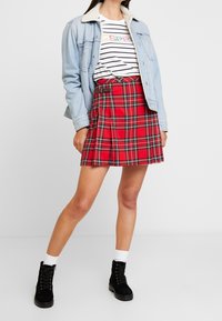 Roter karierter Rock mit Falten, kombiniert mit einem gestreiften T-Shirt und einer Jeansjacke. Schwarze Schnür-Boots ergänzen das Outfit.