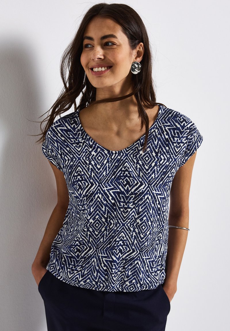 Top a righe blu e bianche con maniche corte, caratterizzato da un design a scollo a V e forme geometriche. Tessuto morbido con una vestibilità comoda.