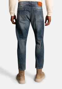 Relaxed-fit, dark blue denim jeans with five pockets, visible stitching, and a leather back patch. Pairing with tan, suede boots.