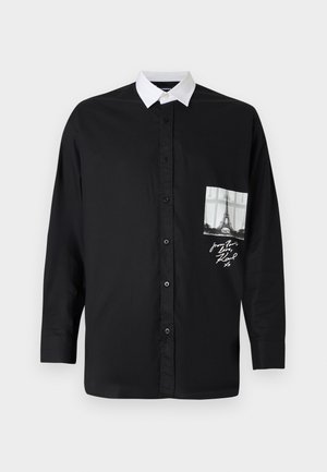 Camisa negra de manga larga con cuello blanco, bolsillo frontal con una impresión en escala de grises de la Torre Eiffel y detalle en script. Textura del tejido suave.