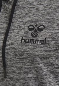 Sudadera gris melange con cordones negros y logo. La tela tiene una textura suave; presenta un patrón sutil y un diseño minimalista.
