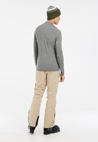 Grijze langemouwen top, beige skibroek met zijritsen, zwarte skischoenen, en een groene gebreide muts met witte strepen.
