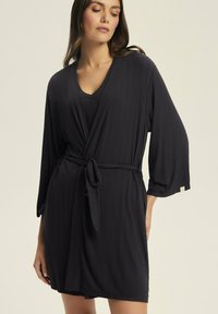 Czarna, prążkowana szlafrok związywany w pasie, z rękawami 3/4 i dekoltem w kształcie V. Gładka tekstura i długość do połowy uda podkreślają jego design.