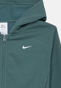 Φούτερ με φερμουάρ Nike Pro σε σκούρο πράσινο-μπλε, με λευκό λογότυπο, απαλό ύφασμα, ριμπ λεπτομέρειες και εφαρμοστή σχεδίαση με κουκούλα.