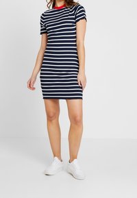 Granatowa i biała sukienka T-shirt w paski z krótkimi rękawami, żebrowana tekstura i czerwona okrągła dekolt, połączona z białymi trampkami.