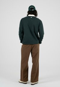 Donkergroen longsleeve shirt met een witte kraag, gecombineerd met bruine wijde broek en crèmekleurige schoenen, gezien vanaf de achterkant.
