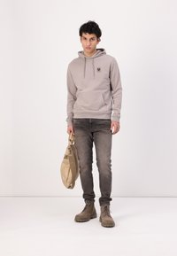 Ανοιχτού γκρι φούτερ με μπροστινή τσέπη και λογότυπο, συνδυασμένο με σκούρα τζιν και μπεζ μπότες. �Το μοντέλο κρατά μια καφέ τσάντα messenger.