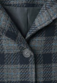 Grå och marinblå rutigt yllekappa med svaga blå fönsterrutor, en stor rund knapp och svart tygfoder inuti kragen.