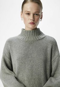 Pull en maille gris clair avec un col côtelé haut, des épaules tombantes et une texture douce. Le design est simple, sans motifs ni accents.