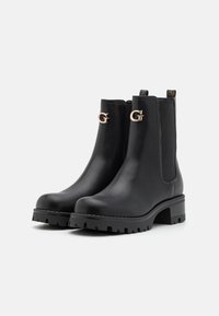 Botas negras de cuero hasta el tobillo con suela de goma gruesa, paneles laterales elásticos y acentos dorados con el logo G en la parte frontal.