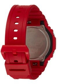Red rubber watch strap with multiple holes and a square buckle. Metal back visible with engraved text, black accents around the case.