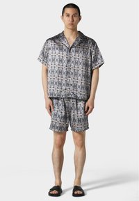 Kurzärmliges, kragenloses Hemd und passende Shorts aus einem graugeprägten Stoff. Das Material hat eine glatte Textur mit einem geometrischen Design.