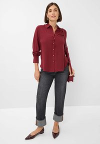 Burgundy button-up shirt with rolled sleeves, paired with dark jeans featuring folded cuffs in gray and brown pattern. Pointed brown flats.