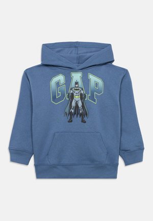 Niebieska bluza z kapturem wykonana z miękkiego materiału, z przednią kieszenią, z grafiką Batmana i napisem "GAP" w jasnej zieleni powyżej.