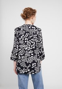 Czarna i biała koszula w panterkę, z rękawami trzyczwartkowymi, luźny krój i zaokrąglony dół. Gładki materiał o subtelnej fakturze.