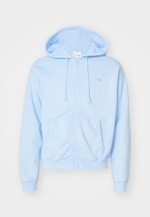 Felpa con zip di colore azzurro chiaro, realizzata in materiale morbido, con cappuccio regolabile, tasche frontali e un piccolo logo sul petto.