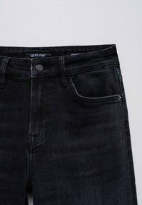 Černé rovné džíny vyrobené z denimu, s knoflíkovým zapínáním, předními kapsami a jemnými švy poblíž pasu.
