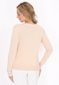 Maglione a maniche lunghe beige chiaro con orlo e polsini a coste, caratterizzato da una sottile texture a maglia e un collo a girocollo con rifiniture bianche.