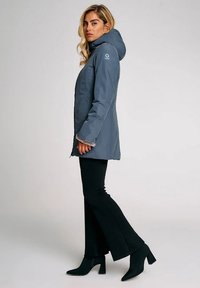 Giacca isolante grigia con cappuccio, dotata di chiusura a zip e bordo in pelliccia sintetica. Abbinata a pantaloni neri a campana e stivali con tacco.