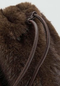 Primer plano de un material de pelo suave marrón oscuro con dos cordones de cuero negro cosidos sobre un fondo claro.