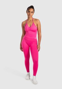 Completo sportivo rosa composto da un top halter aderente con dettagli arricciati e leggings a vita alta coordinati, entrambi realizzati in un materiale liscio e elasticizzato.