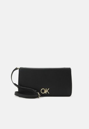 Schwarze rechteckige Crossbody-Tasche mit verstellbarem Riemen und goldfarbenem Calvin Klein Logo auf der Vorderseite vor weißem Hintergrund.