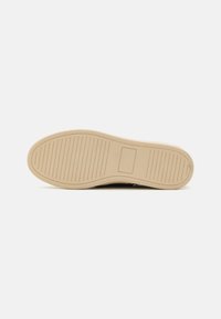 Shoe outsole featuring a beige rubber material, textured surface with grooves, and a rectangular logo patch near the heel.