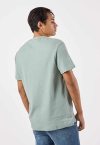 Ljusgrön ribbad T-shirt med korta ärmar, rund halsringning och sidenskärningar, kombinerad med blå jeans.